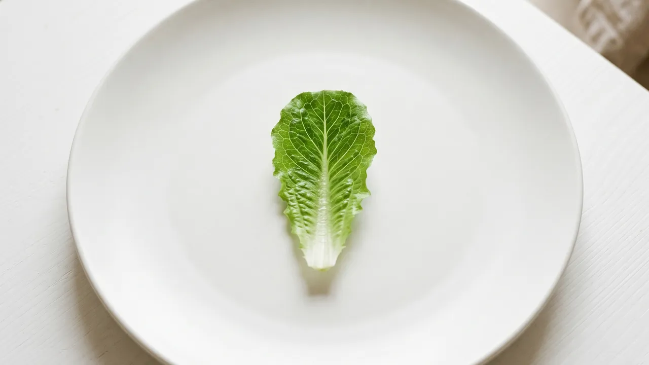 Assiette avec une feuille de salade isolée symbolisant la restriction d'un régime, fond blanc épuré